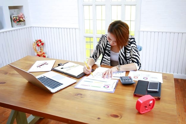 A person sitting at a desk, reviewing and organizing tax documents, including forms 8949 and Schedule D, with a laptop displaying cryptocurrency transaction records in the background.